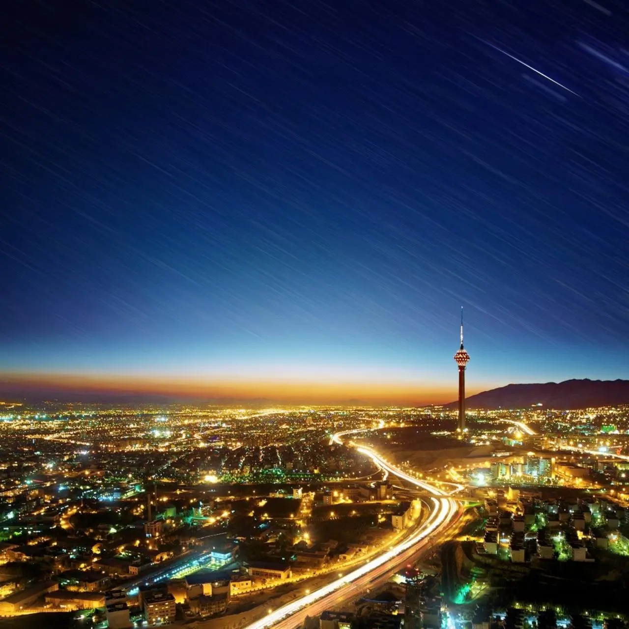 تهران در شب زیر آسمانی با رد ستارهها در عکاسی نوردهی طولانی، با برج میلاد در افق